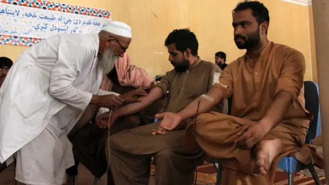 Two men have their blood taken by a man wearing a long white lab coat