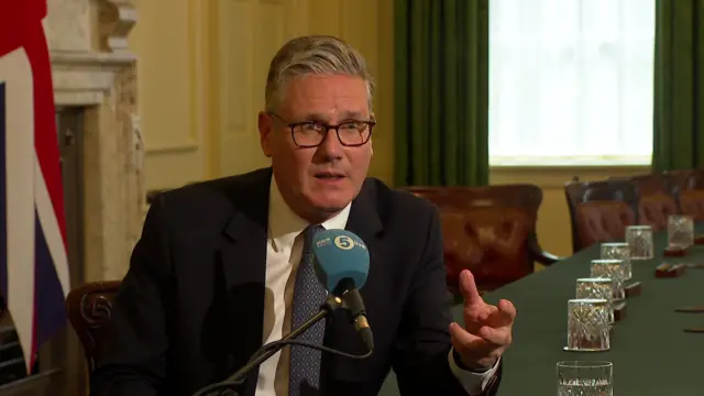 Starmer speaking into a 5Live microphone sitting at the cabinet table, flanked by a union flag