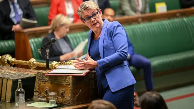 Yvette Cooper, in a blue blazer, speaks at the despatch box with a pen in hand