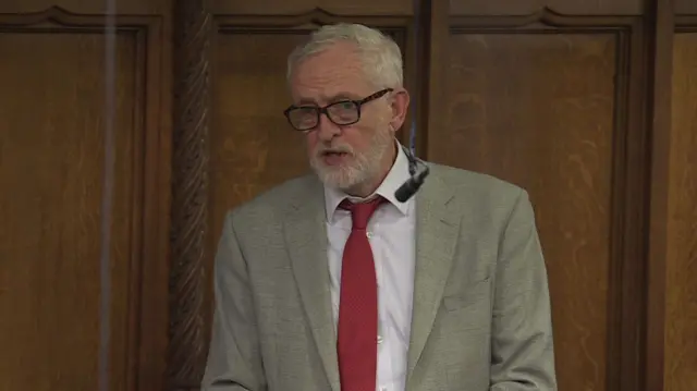 Corbyn in red tie and beige blazer addressing Commons