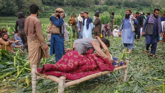 A man hugs another man who is on a makeshift stretcher in a field