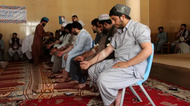Men sit in a line giving blood in an arm