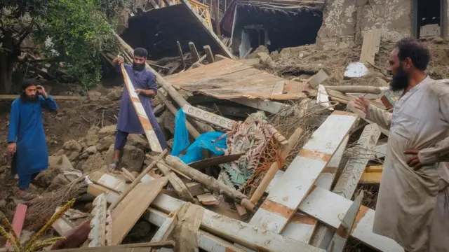 Three men look through a large pile of rubble
