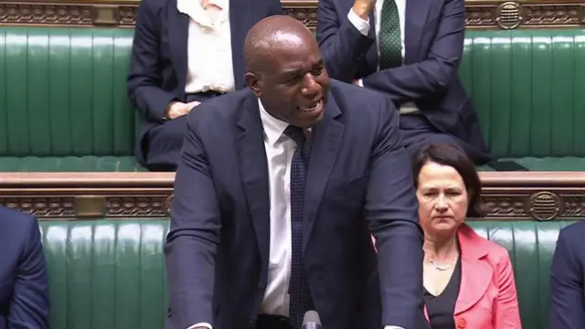 David Lammy in a navy suit in front of the green benches of the commons