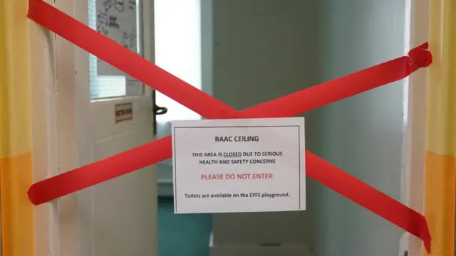 A barrier across a door with a sign saying the ceiling as Raac and the area is closed