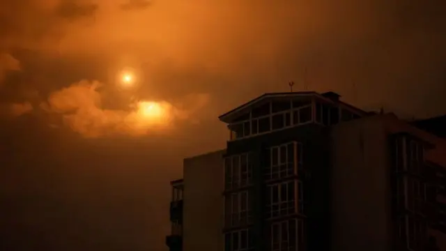Two fireballs light up the orange sky above a residential building.