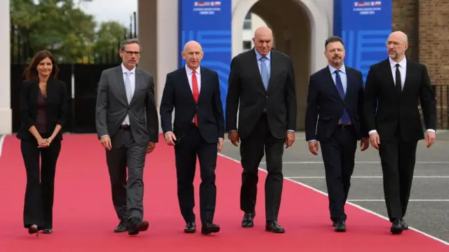 Six people, five men and one woman, dressed smartly and walking together down a red carpet