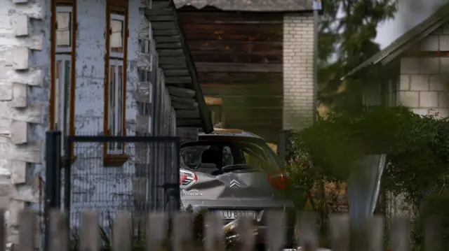 Car in the distance that is dented by a drone. It is surrounded by buildings