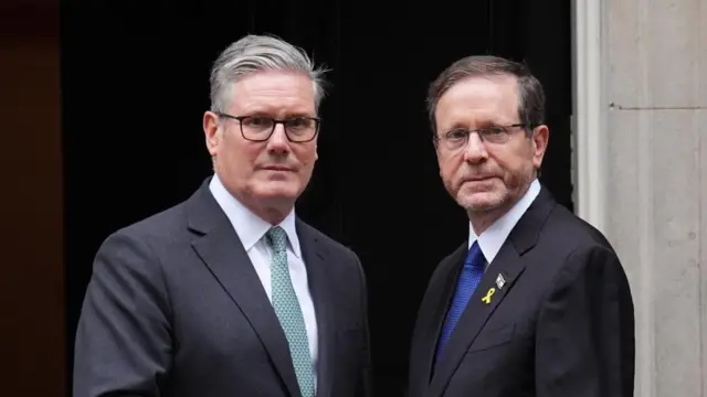 UK PM Keir Starmer stands beside Israeli President Isaac Herzog. They both wear suits and glasses.