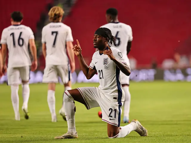 Noni Madueke kneels down and holds up a finger to celebrate scoring a goal