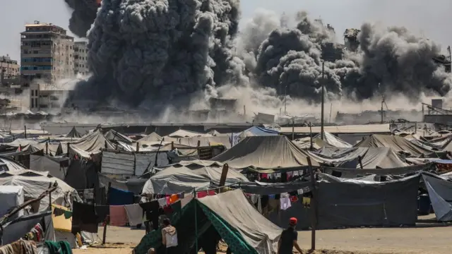 Gazans emerge from tents to watch enormous plumes of black smoke rise from the site of an israeli strike nearby