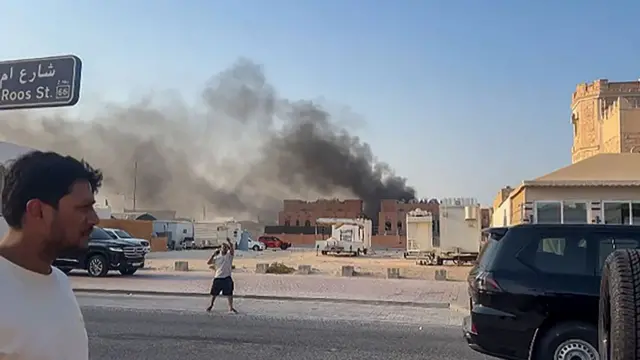 Smoke billowing from a building while a man walks by on the street