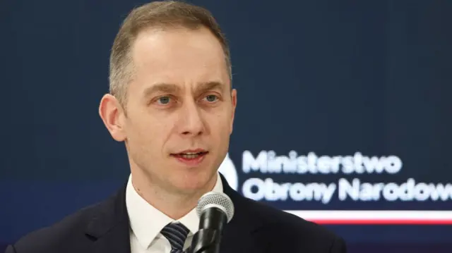 Poland's Deputy Defence Minister Cezary Tomczyk standing at podium in dark suit