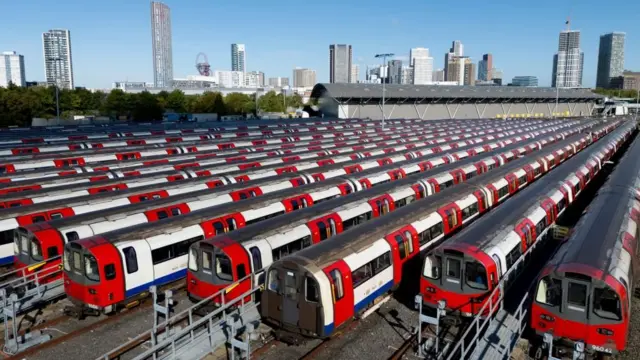 About 15 Underground trains are seen lined up in a depot in front of the East London skyline