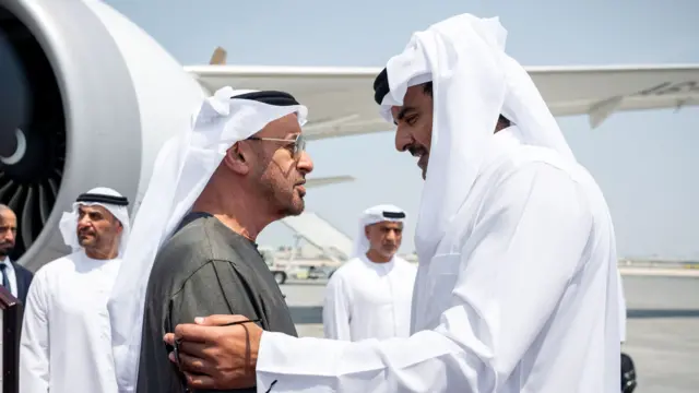 two men in white and grey clothing stand face to face on tarmac in front of a plane