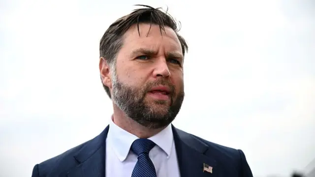 JD Vance wearing a navy suit with a US flag pin on his collar