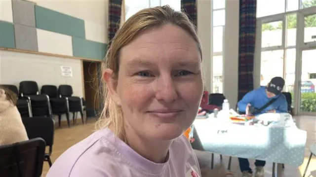 A woman with dark blonde hair tied back, wearing a pink shirt