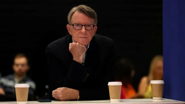Man in black blazer sits with his chin resting on a propped hand