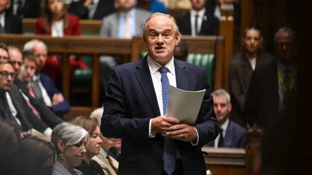 Man in blue suit speaks in Parliament surrounded by people