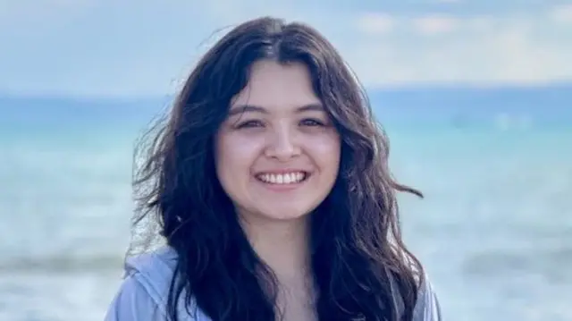 Tiana Lao smiling into the camera. She is stood on a beach, in front of the sea.