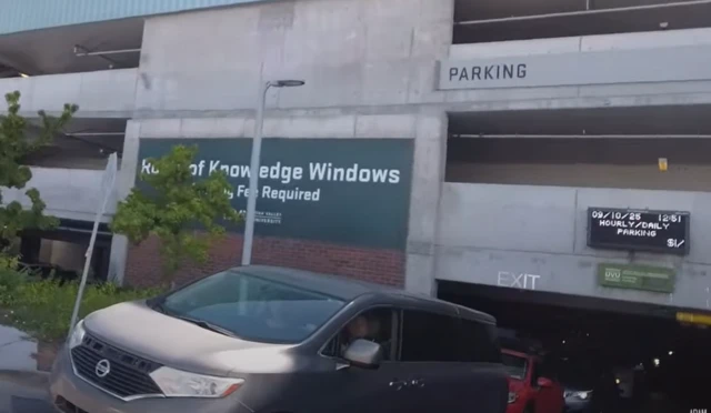 A screenshot from a video showing a digital clock at the edge of a digital display on the side of a car park wall