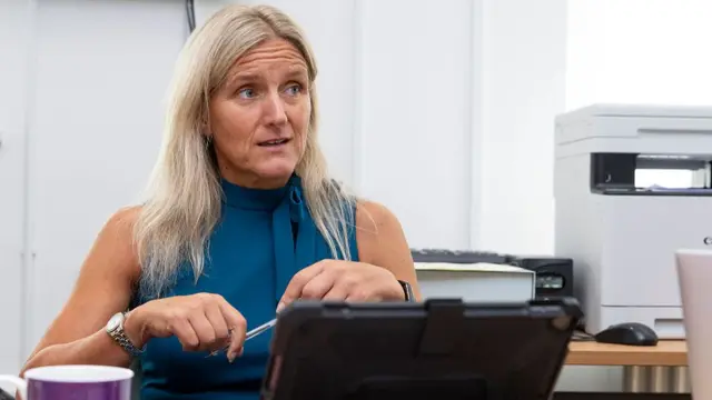 Kim Leadbeater with long blonde hair and a blue sleeveless blouse, sitting at a desk in front of an iPad.