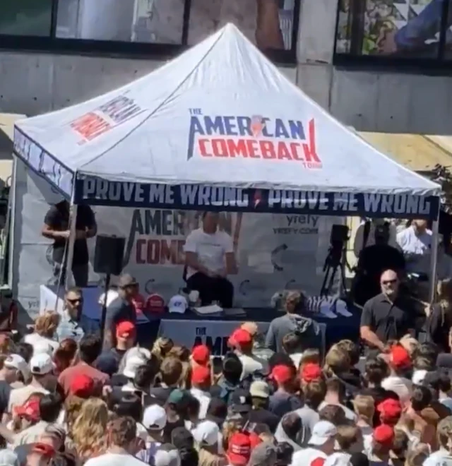 Kirk sitting underneath a marquee in front of a large crowd of people