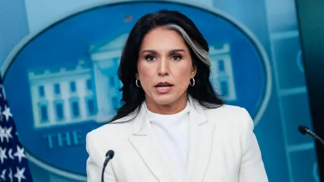 Brunette woman in a white blazer speaking into a mic