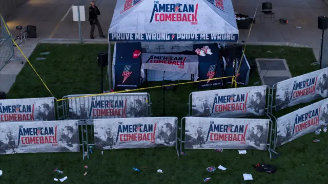 A drone view shows the tent which is branded with the words AMERICAN COMEBACK. Some branded merchandise hats are still on the table in the tent. There are barriers around the tent that also read AMERICAN COMEBACK. There is litter around the grass