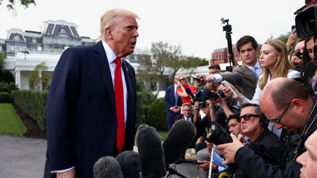 Trump speaks to a gaggle of reporters, many crouching and holding out microphones and cameras