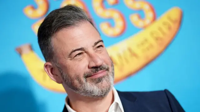 Jimmy Kimmel, smiling and looking off camera to the right, in a dark blue suit