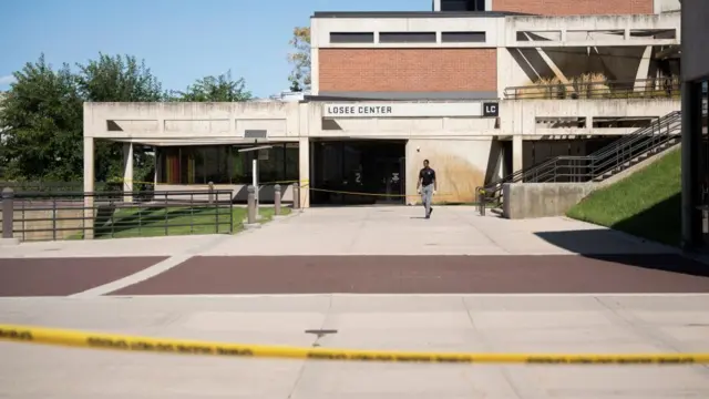 An official walks in front of a building named the Losee Center at the Utah Valley University. Police tape cordon off two areas.