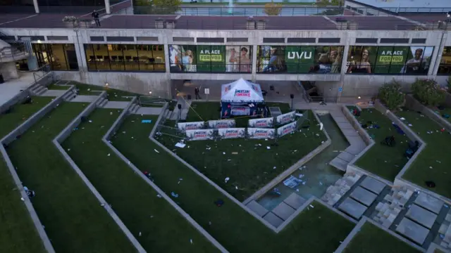 A drone view of a campus, with a tent and signs reading 'American comeback'. Belongings are strewn across the grass.