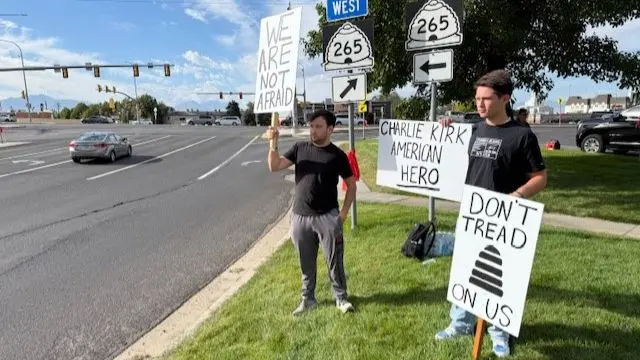 Two young men holding three signs, one saying 'don't tread on us', another 'we are not afraid' and another 'Charlie Kirk American Hero'