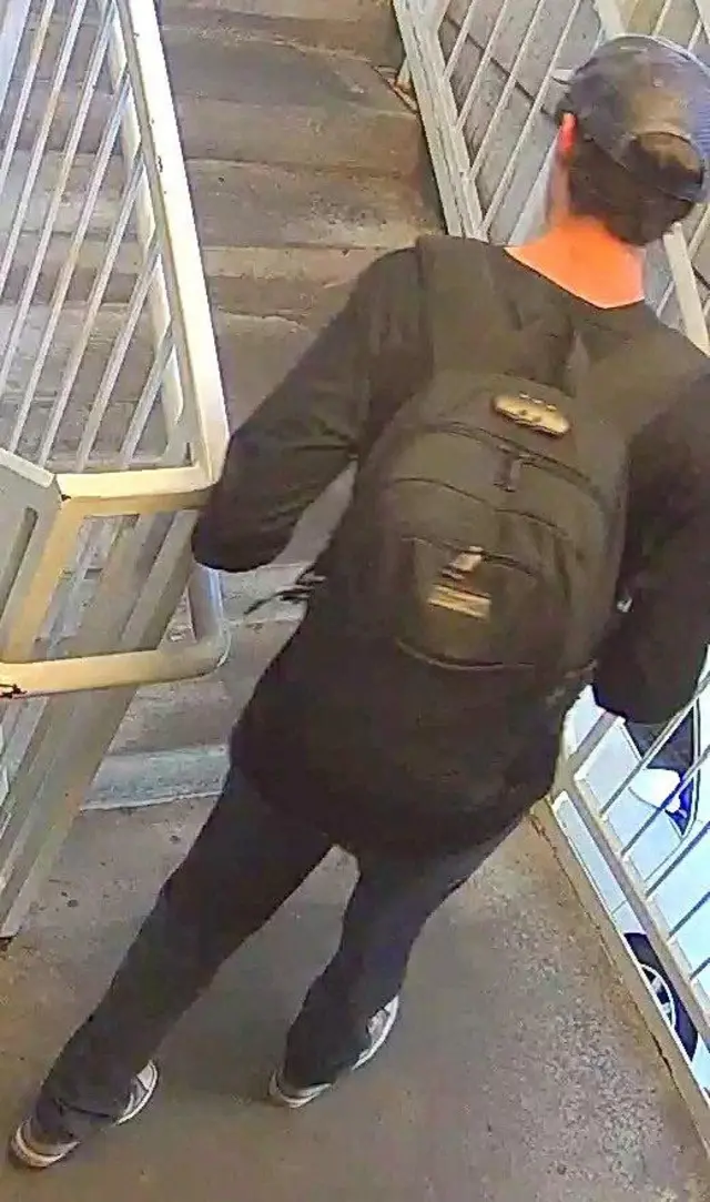 Person of interest in connection with the killing of Charlie Kirk walking up a flight of stairs. He has his back to the camera, is wearing all black and is carrying a black rucksack. He has a dark blue baseball cap on