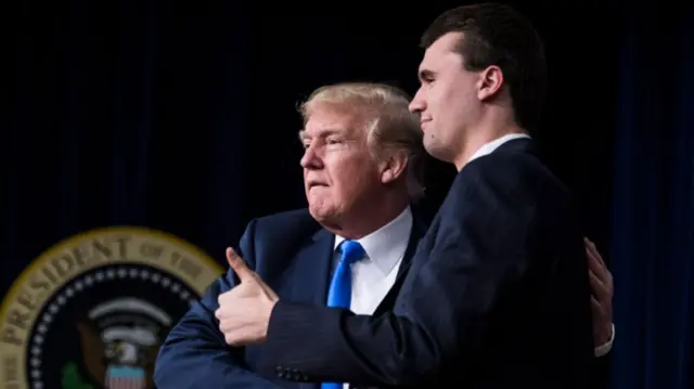 Donald Trump and Charlie Kirk embrace while Kirk holds his thumb up on stage