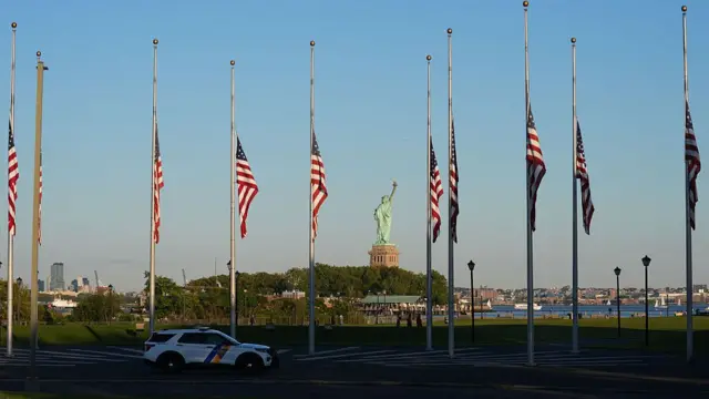 Ten US flags flown at half mast in honour of Charlie Kirk. The Statue of Liberty can be seen in the background.