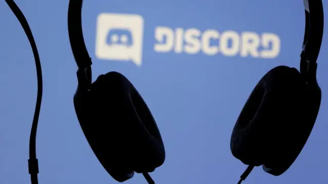 Headphones are seen in front of displayed Discord app logo