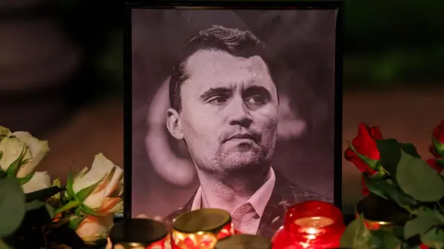 Framed photograph of Charlie Kirk with flowers either side of it. There are some red candles in front