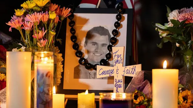 A picture of Charlie Kirk lays in the middle of a memorial with candles and flowers around it