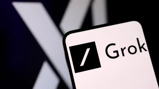 Close up of a phone screen displaying the Grok logo. The logo for X is partially visible on a black background behind the phone