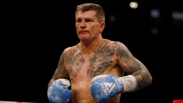 Ricky Hatton stands shirtless on the ring wearing blue boxing gloves