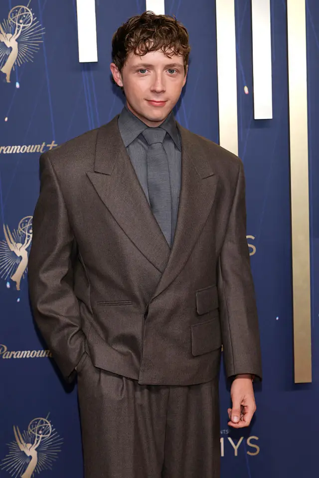 Gerran Howell in a loose grey suit poses on the red carpet