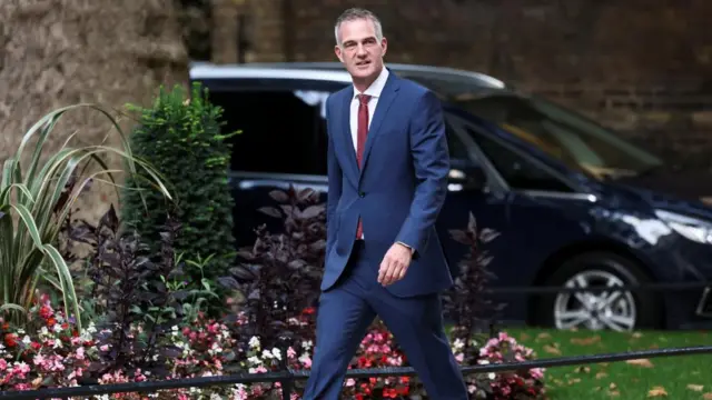 Peter Kyle in a blue suit and red tie walking down Downing Street.