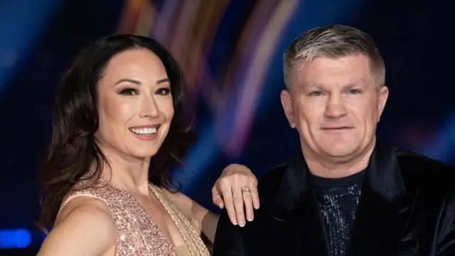 A woman with brunette hair and a sparkly dress next to Ricky Hatton in a black suit