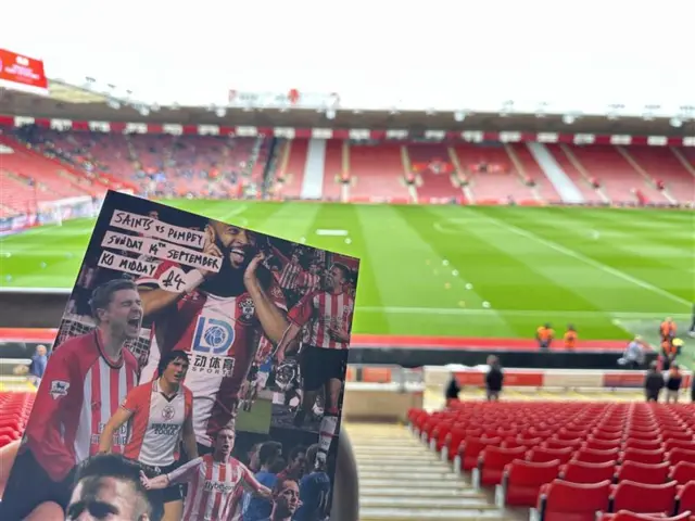 A matchday programmes for Southampton v Portsmouth being held up in front of a view of the seats and pitch at St Mary's