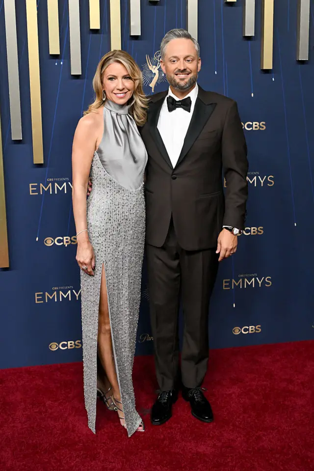 Nate Bargatze walks the carpet in a black tuxedo with his wife Laura Bargatze, who wears a silver dress