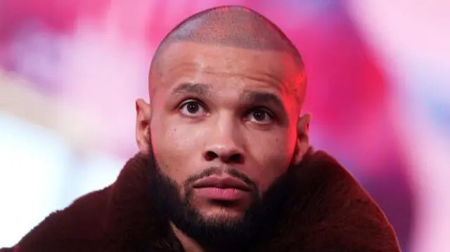 Chris Eubank in a black coat in front of a pink background