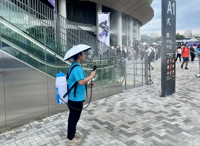 A volunteer helps spectators cool down with mist