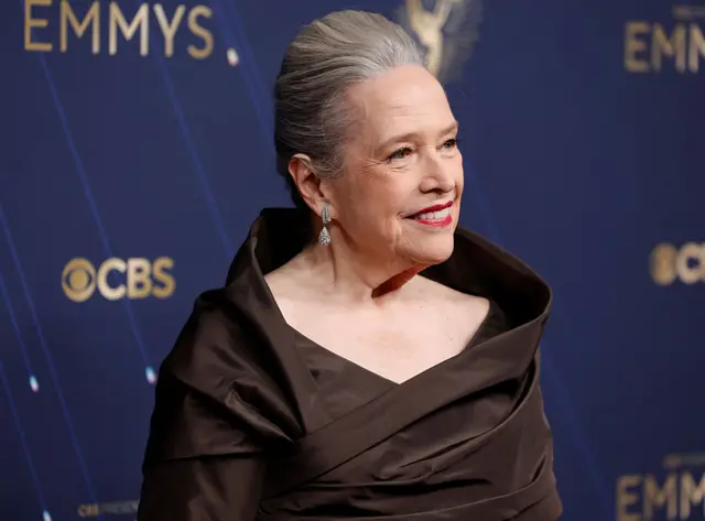 Kathy Bates walks the carpet in black dress with long sleeves.